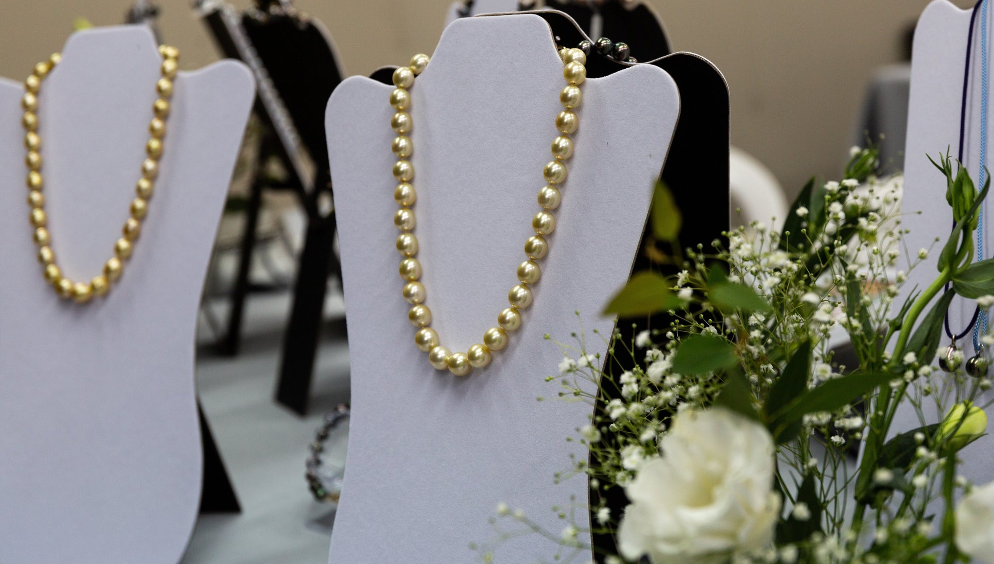 Gold necklaces on white stands with a floral arrangement in the foreground.