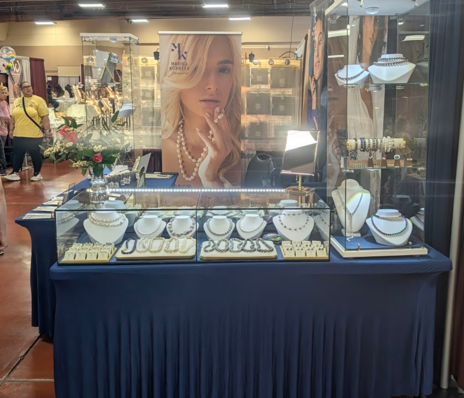 Jewelry display table with various items at an event, featuring a Marina Korneev Fine Pearls banner.