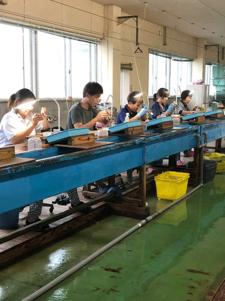 Assembly line workers crafting cultured pearls at a blue workbench, debunking myths.