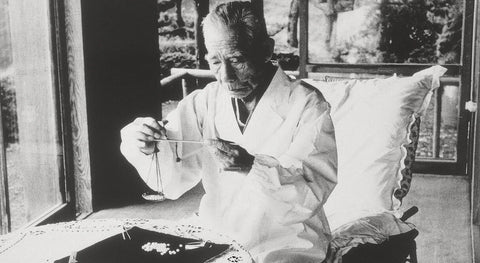 Black and white photo of a person examining Mikimoto Pearls in a white robe.