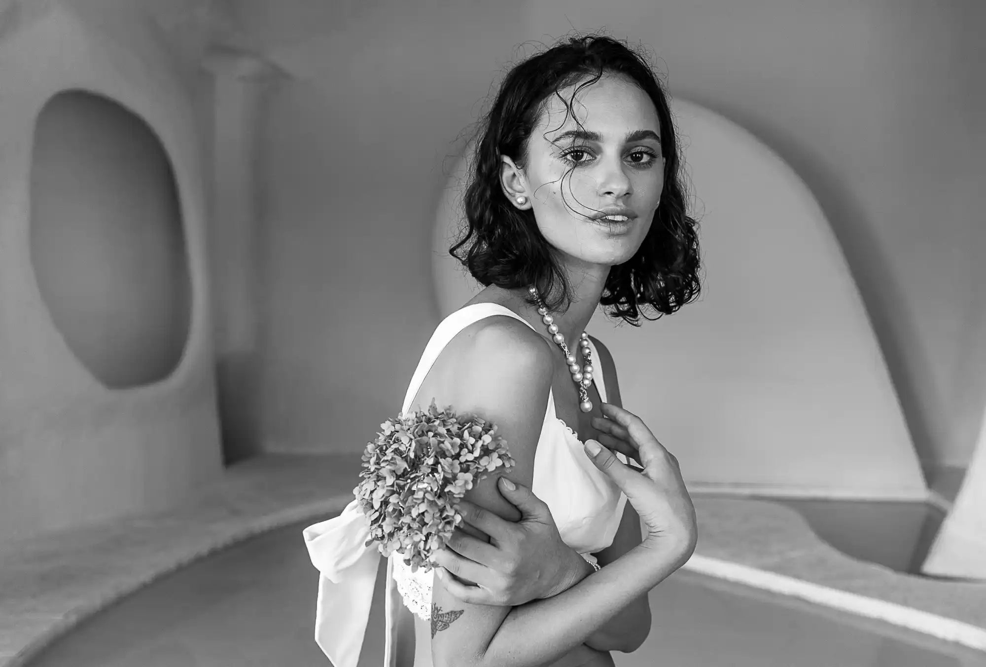 Black and white portrait photograph of someone in a white dress holding flowers.