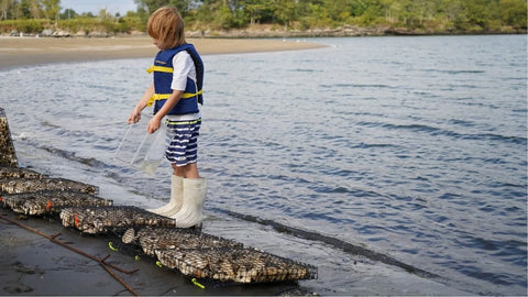 Child in life vest and boots by water to promote ocean health and responsible pearl farming.