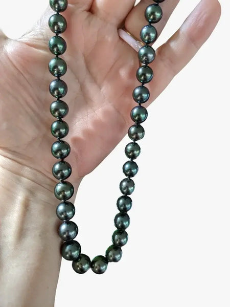 Dark green-black Tahitian pearls showcasing surface quality in a hand, Marina Korneev Pearls.